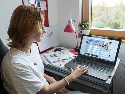 Eine junge Frau sieht sich zuhause die Website planet-beruf.de auf dem Laptop an.