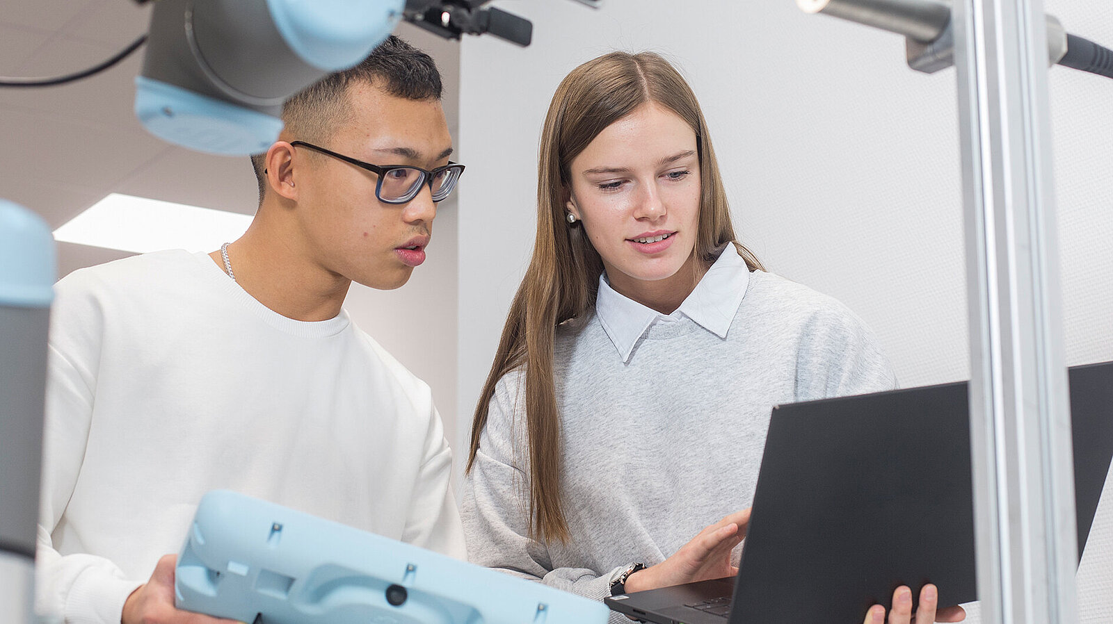 Eine Frau und ein Mann arbeiten in einem technischen Labor an einem Laptop.