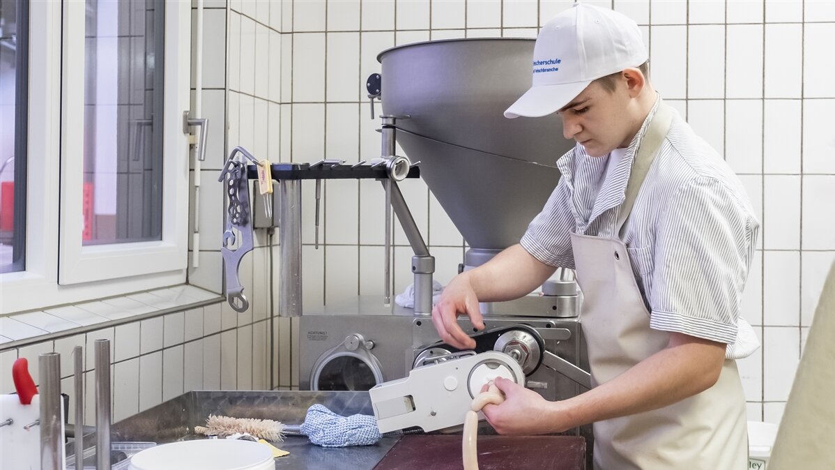 Stefan steht an der Füllmaschine und füllt Würstchenmasse in Därme ab.