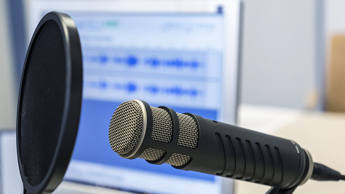 Ein Profi-Mikrofon zur Tonaufnahme und ein PC-Bildschirm mit einem Audioprogramm.