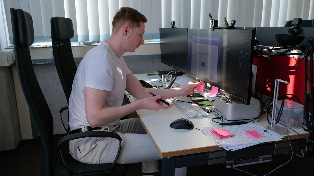 Ein junger Mediengestalter klebt kleine Post-its auf den Monitor.