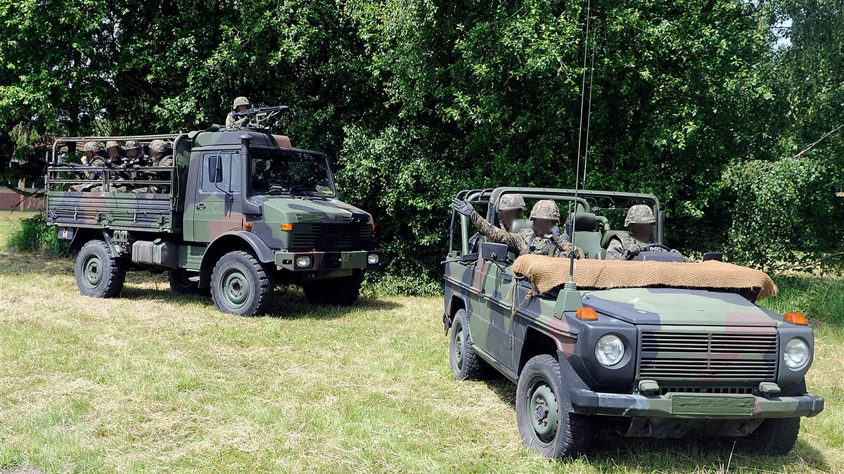 Zwei Tarnfahrzeuge der Bundeswehr stehen auf einer Wiese. In beiden Fahrzeugen sitzen Soldaten in Tarnuniformen und Helmen.