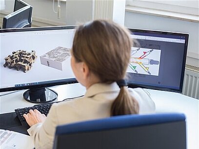 Eine junge Frau arbeitet an einem Comuter mit zwei Bildschirmen.