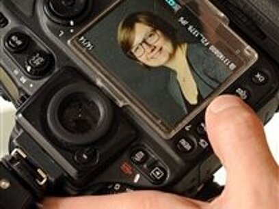 Zwei Hände halten eine Fotokamera, auf der ein Porträtfoto einer lächelnden Frau zu sehen ist.