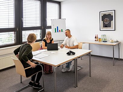 Zwei junge Frauen und ein junger Mann sitzen an einem Tisch in einem Besprechungsraum.