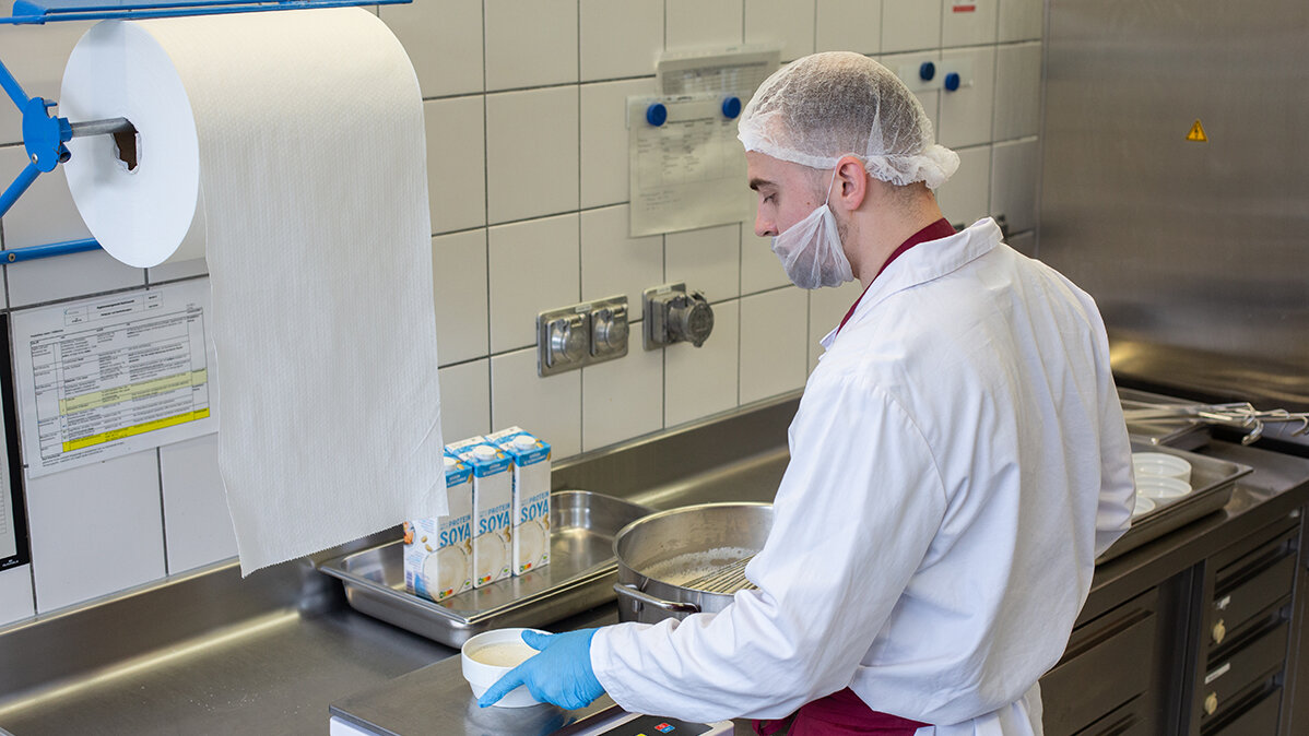 Ruben steht in Arbeitskleidung im Kühlhaus und wiegt Essen ab.