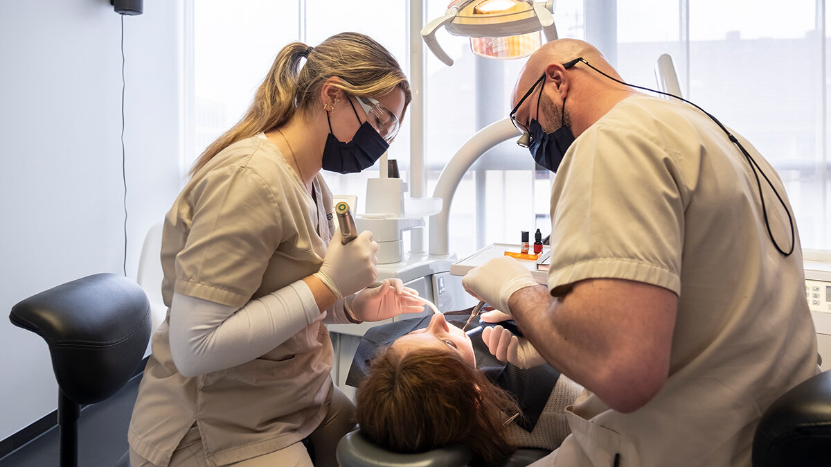 Karolin trägt Schutzausrüstung und assistiert dem Zahnarzt im Behandlungszimmer bei einer Füllung.