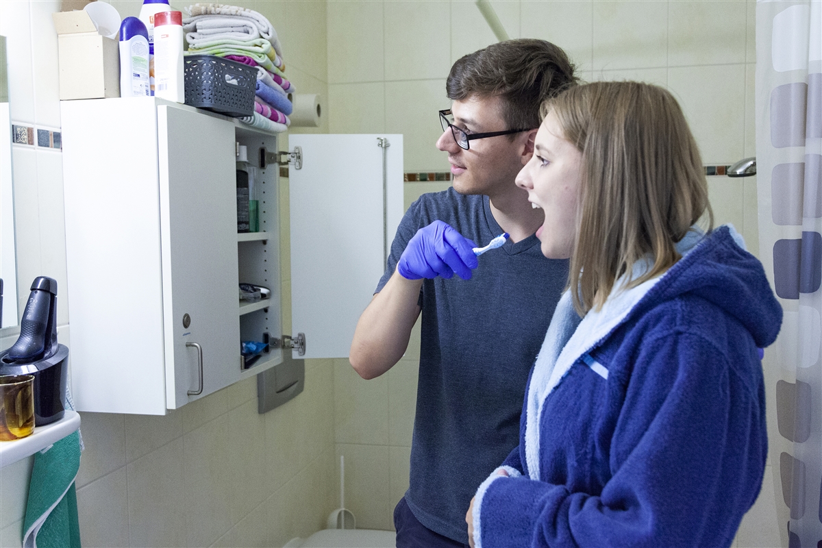 Ein junger Mann hilft einer jungen Frau beim Zähneputzen.
