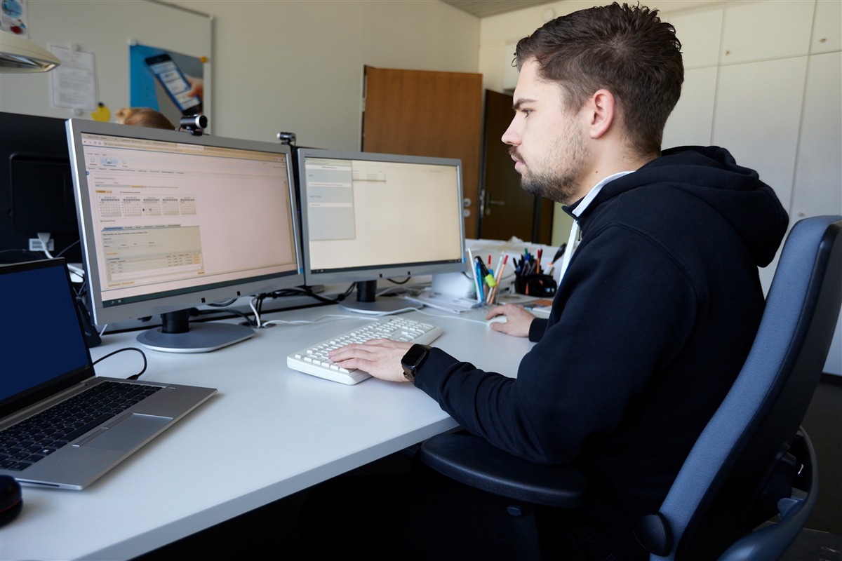 Ein junger Mann arbeitet mit zwei Bildschirmen am Computer.