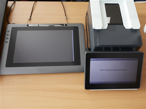 Ein Dokumentenscanner, ein Tablet und ein Drucker liegen auf einem Tisch.