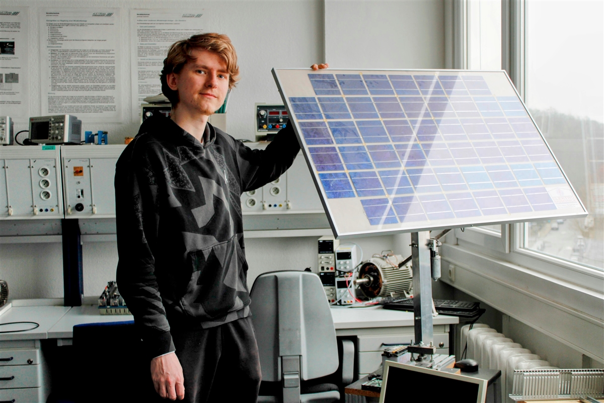 Jason steht in einem Büro und zeigt ein Solarpanel.