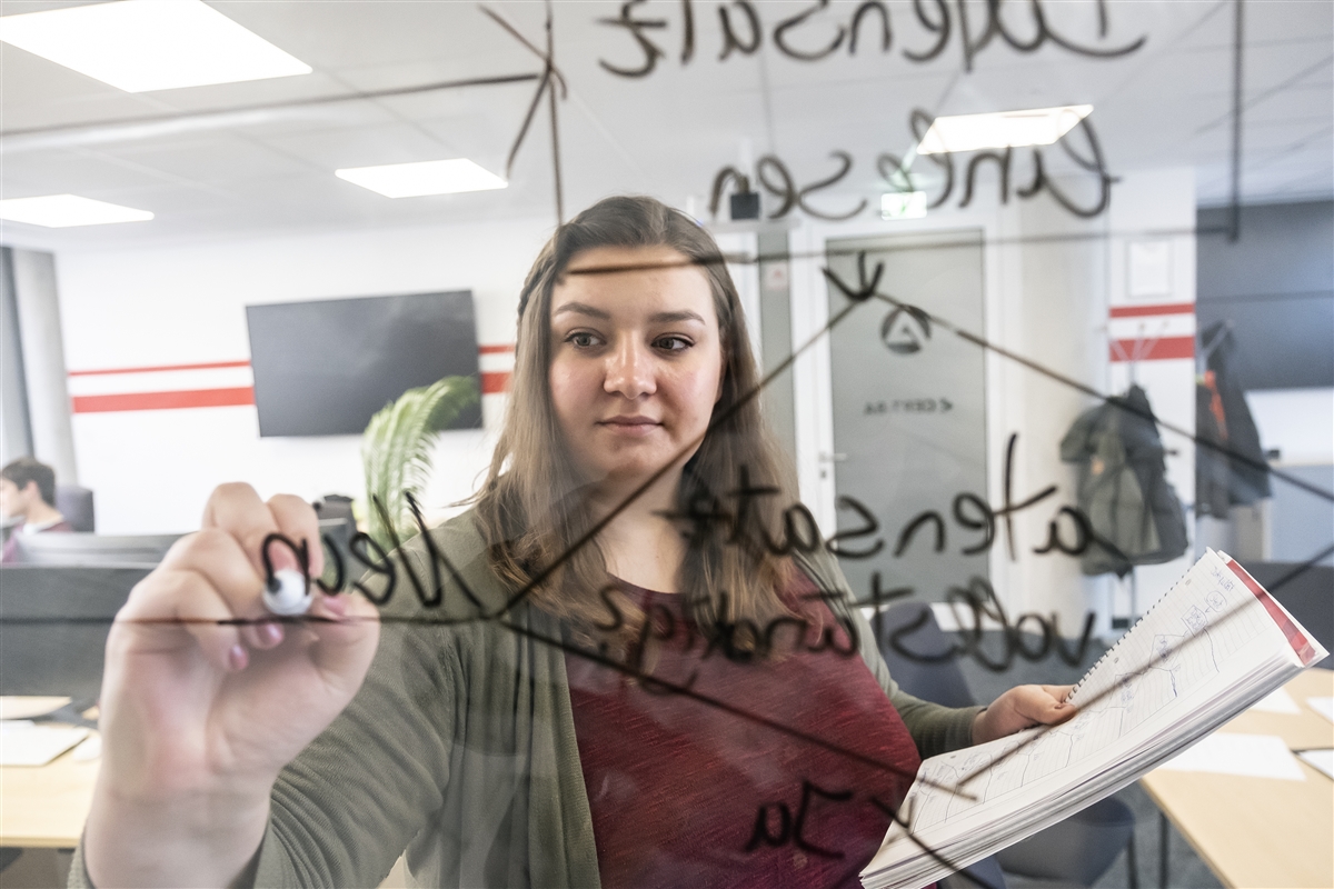 Sonja schreibt einen Prozessablaufplan auf ein Glasboard.