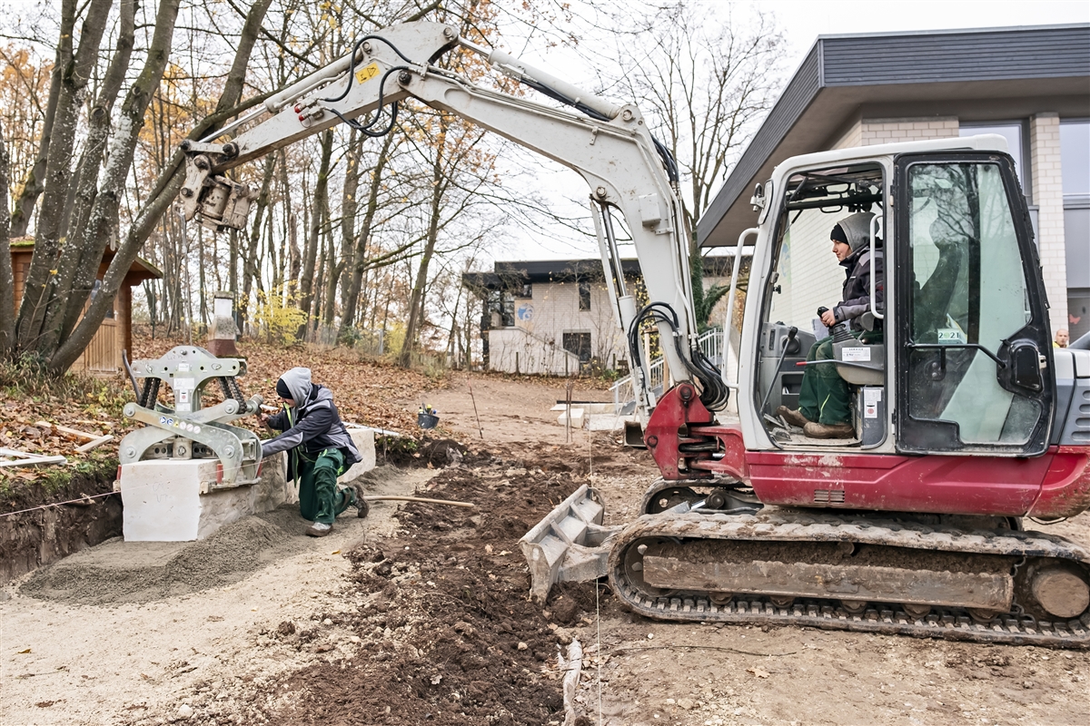Hannah bewegt große Mauersteine mit dem Bagger, Marcel setzt sie an die richtige Position.