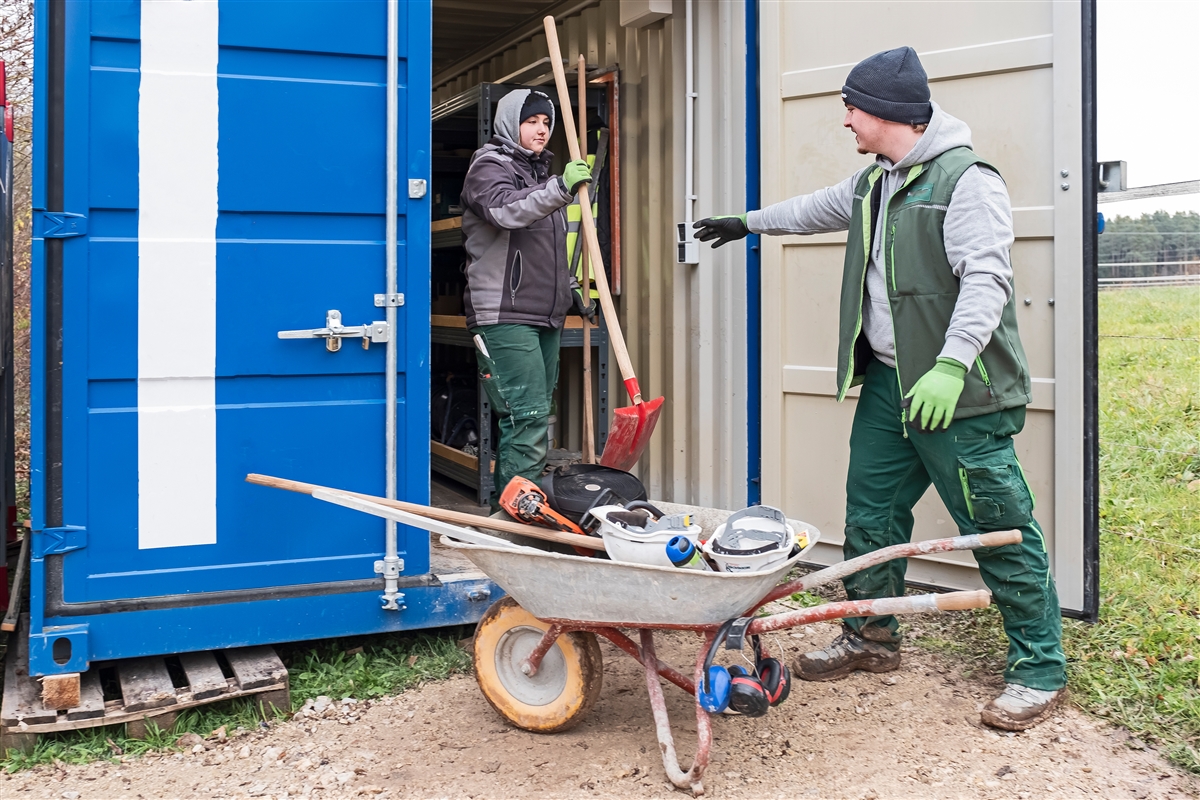 Hannah und Marcel holen Werkzeuge und Geräte aus einem Container.
