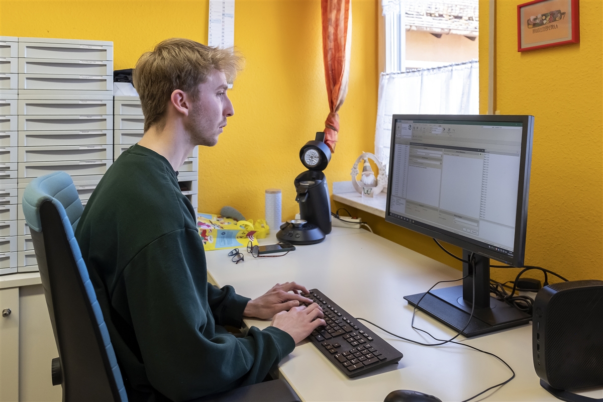 Moritz sitzt am Computer und schreibt auf, was die Klientinnen und Klienten gemacht haben.