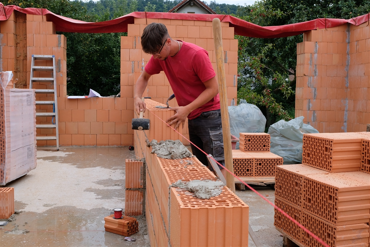 Adriatik klopft auf der Baustelle einen Ziegelstein auf einer Mauer mit dem Gummihammer in die richtige Position.