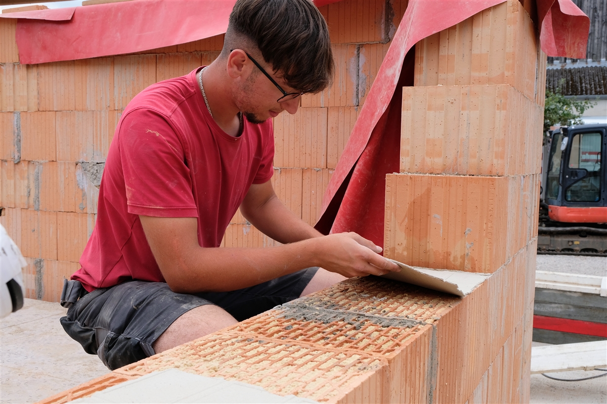 Adriatik legt auf einer Baustelle ein Mörtelpad auf eine Mauer aus Planziegeln.