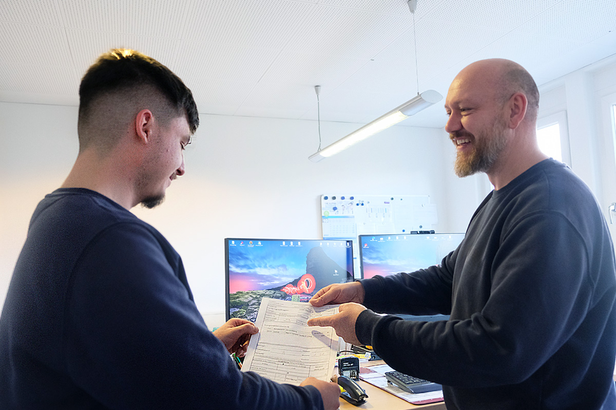 Der Produktionsleiter zeigt Maciej den heutigen ausgedruckten Arbeitsplan.
