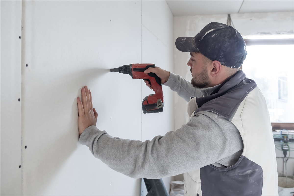 Max verschraubt mit einem Akkuschrauber Gipskartonplatten an einer Trockenbauwand.