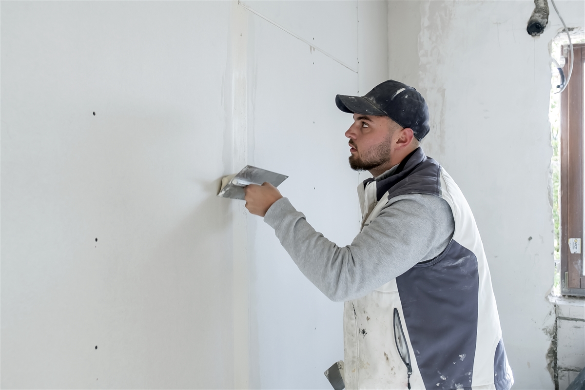Max verspachtelt mit dem Spachtel die Schrauben an einer Trockenbauwand.