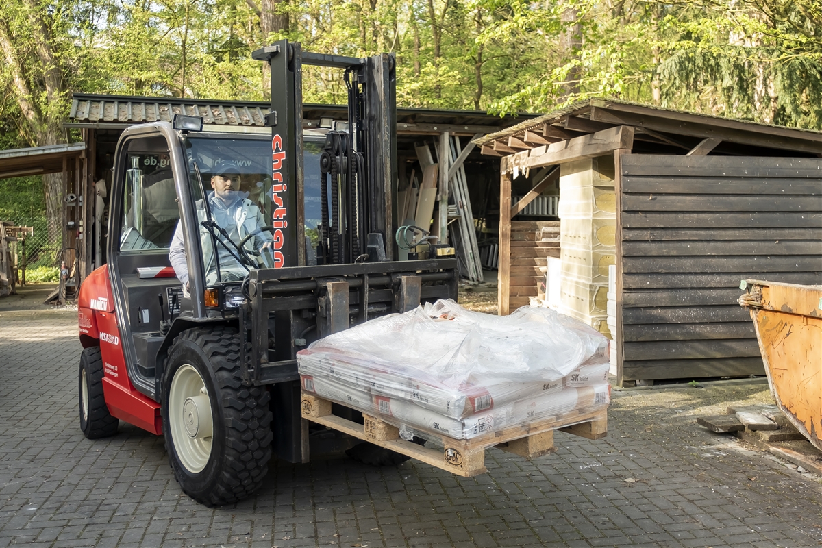Max transportiert im Lager eine Palette mit Baumaterial mit einem Gabelstapler.