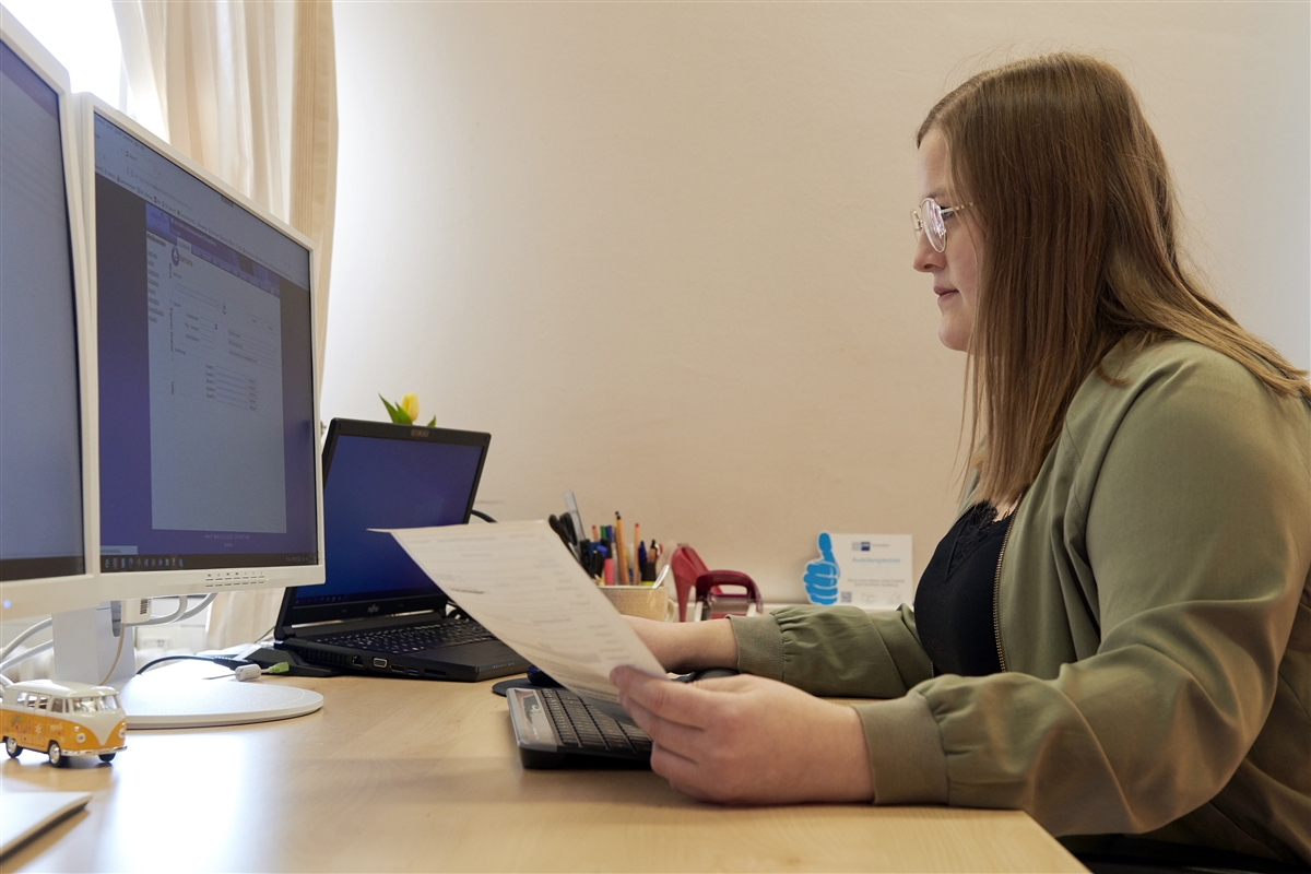 Tina kontrolliert eine Rechnung und überträgt sie ins Rechnungsprogramm am Computer.