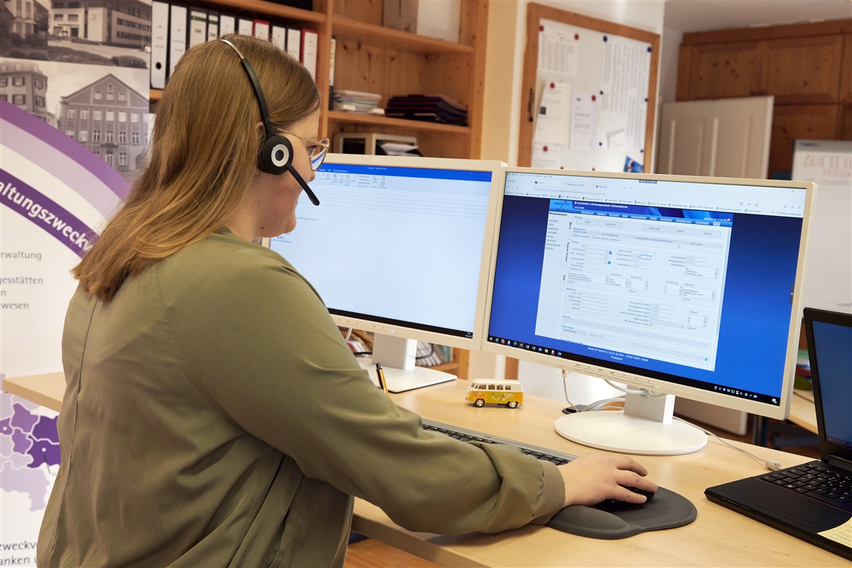Tina telefoniert per Headset mit einem Gemeindemitglied und erstellt den Patenschein am Computer.