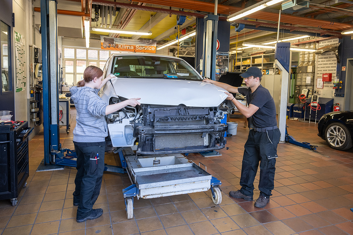 Zwei junge Menschen entfernen die Motorhaube eines Autos.