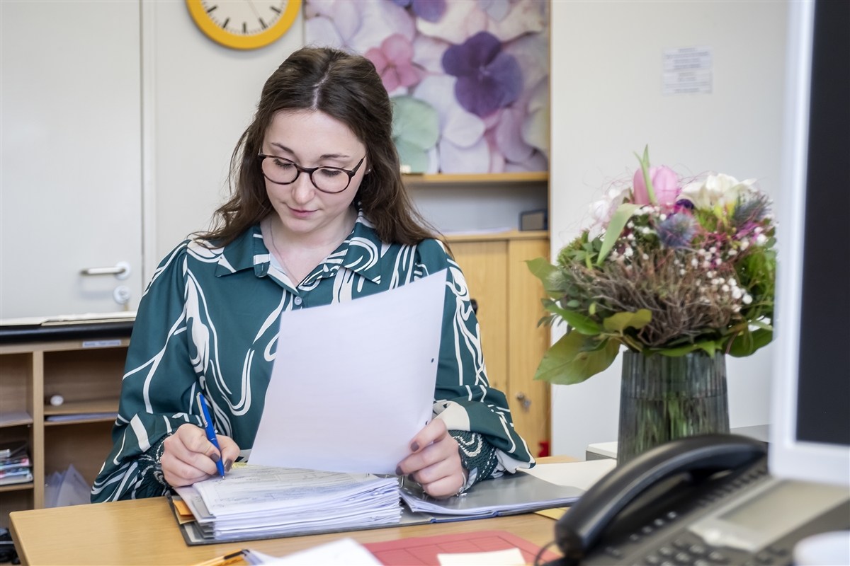 Vor Laura liegt ein Ordner auf dem Schreibtisch, in dem sie Anträge bearbeitet.