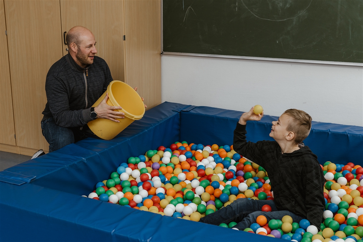 Ein Junge im Bällebad und ein Mann spielen zusammen.