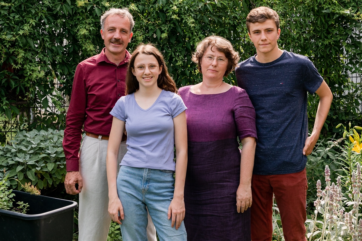 Eltern mit Sohn und Tochter stehen im Freien und schauen in die Kamera.