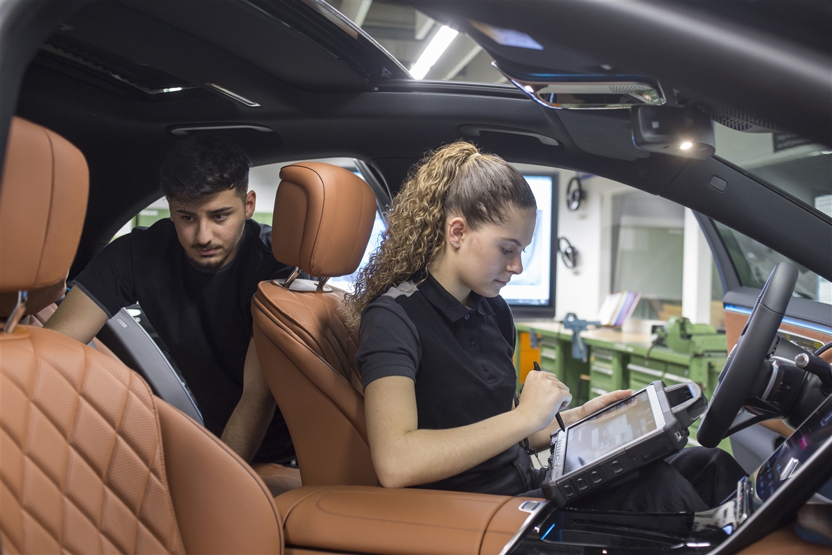 Eine junge Frau schreibt im Innenraum eines Autos auf einem Tablet während ein junger Mann die hintere Sitzreihe überprüft.