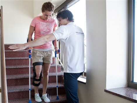 Ein Mann hilft einer Frau mit Krücken dabei, eine Treppe herunterzulaufen.